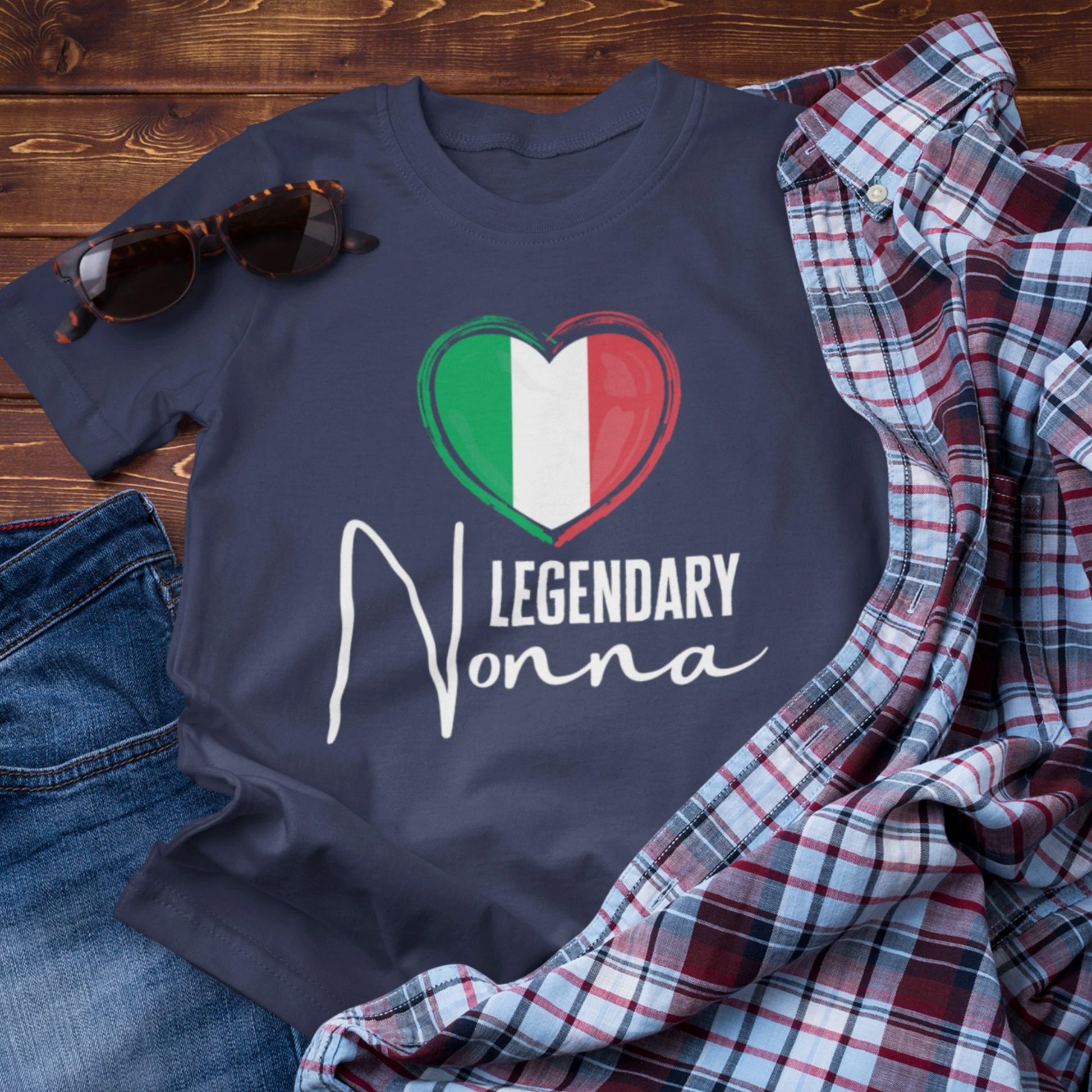 Navy blue t-shirt with 'Legendary Nonna' design on a wooden surface with jeans, sunglasses, and a plaid shirt.